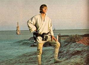 Luke Skywalker (Mark Hamill) auf seinem Heimatplaneten Tatooine. Hinter ihm ist ein Vaporator zu sehen, der genutzt wird, um das lebensfeindliche Wüstenland zu bewässern. Anstatt ihn zu reparieren, beobachtet Luke einen Kampf im Weltraum.